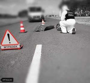 Znak informacyjny &quot;Wypadek&quot;, a w tle technik kryminalistyki bada ślady wypadku drogowego.
